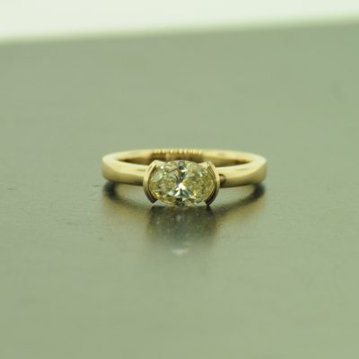 Oval diamond set in yellow gold half bezel engagement ring. By Marcus Ó Broin Jewellery, Kelowna, BC